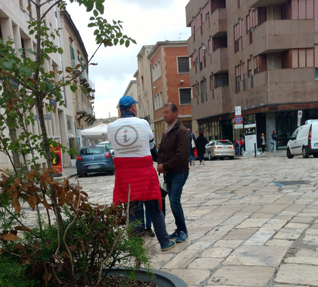 Sei su: Come proteggersi dalle trappole per turisti a Matera. Immagine con falso dipendente comunale che indossa una maglietta con il simbolo delle informazioni turistiche.